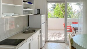 Cocina pequeña con fregadero, microondas y refrigerador. Unas puertas corredizas de vidrio dan a un balcón con mesa y sillas.