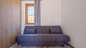 A modern living room with a grey sofa, wooden panel wall, and a window with curtains. - Il Piccolo Borghetto - Guest House Stazione Tiburtina (Roma)