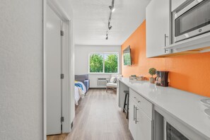 A modern kitchen with white cabinets, a microwave, and a window with a view of trees. - Chic 1-bedroom Micro Studio Apartment (Cedar Falls)