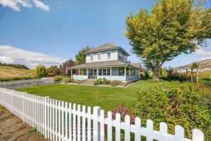 A two-story house with a porch, surrounded by a white picket fence, a well-maintained lawn, and a large tree. - Meadowsweet Farm by WanderLodges (Medford)