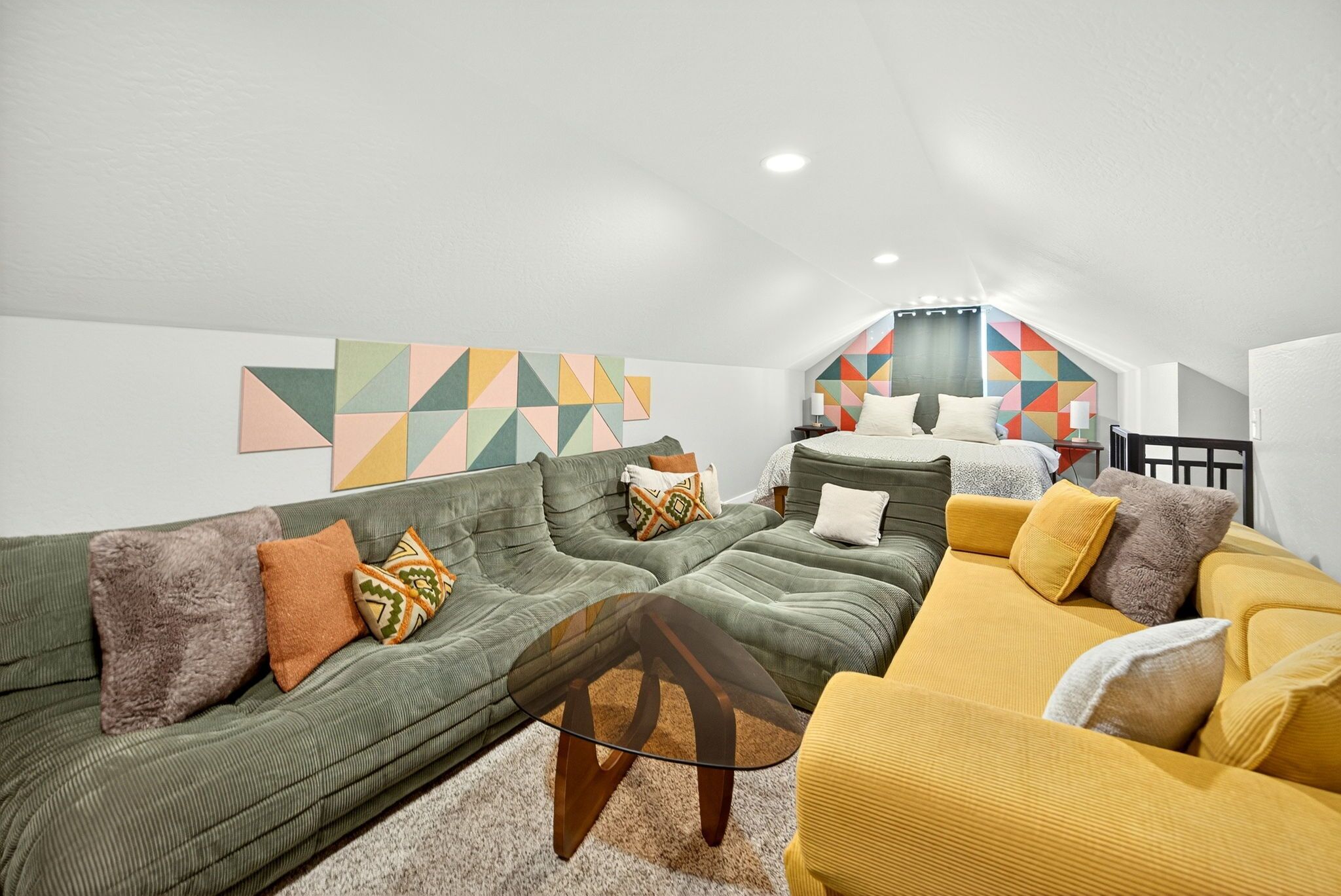 Ett modernt sovrum i loftstil med en stor säng, en grön soffa, en gul soffa och ett geometriskt konstverk på väggen.