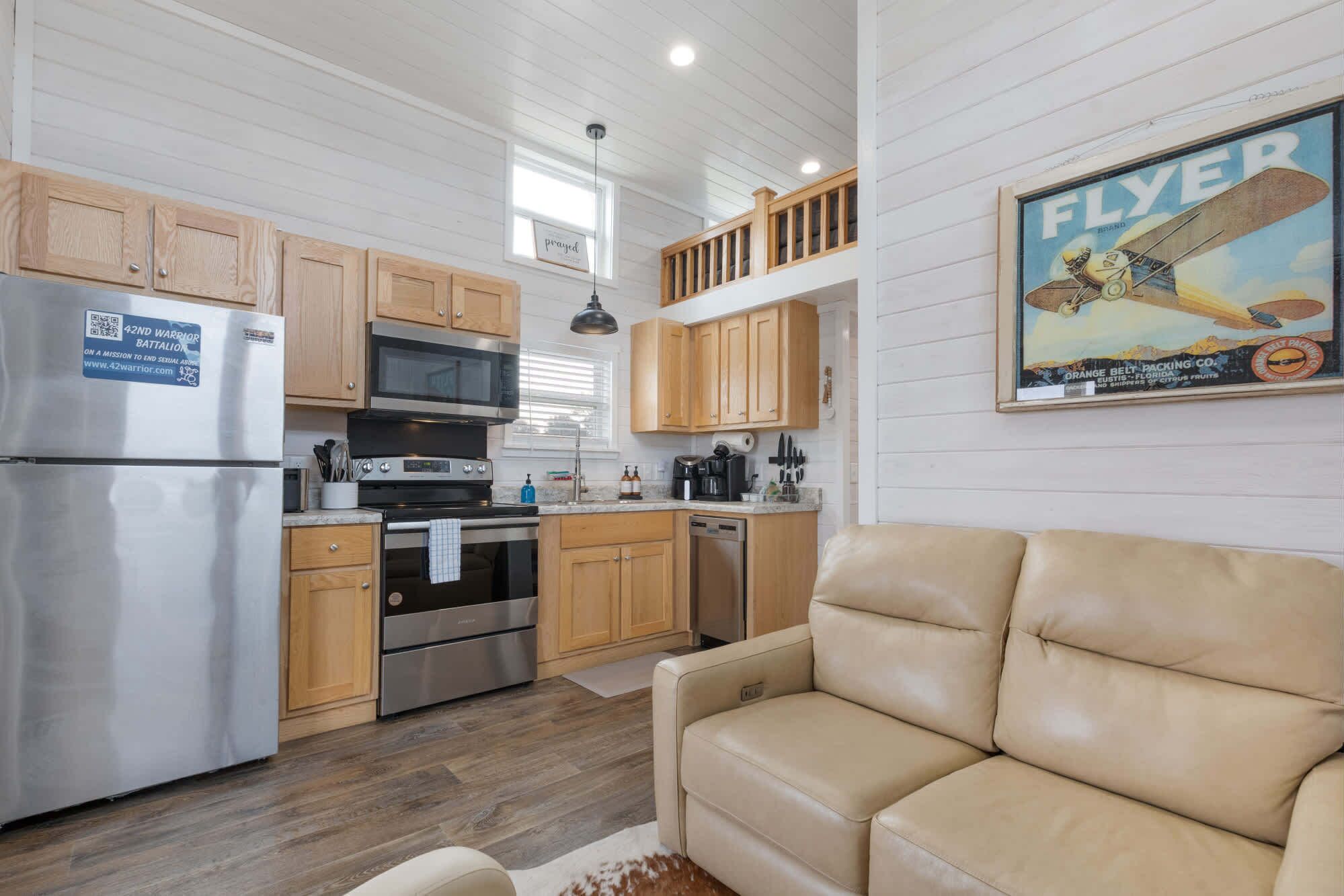 A compact kitchen with wooden cabinets, stainless steel appliances, and a beige leather sofa.