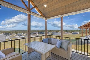 A covered outdoor deck with a table and seating, overlooking a residential area.
