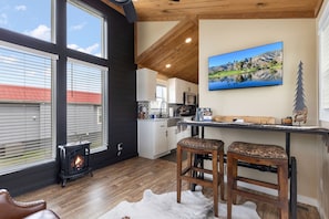 Ein gemütliches Interieur mit Kamin, Holzböden, einer Küche mit weißen Schränken und einem großen Fenster.