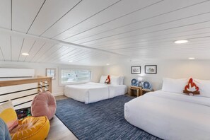 Habitación de hotel con dos camas, una litera de madera, un escritorio, dos ventiladores de pared y una ventana con persianas.