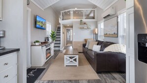 A spacious living area with a fireplace, a sofa, a TV, and a staircase leading to an upper level.
