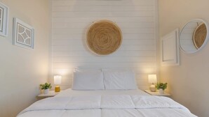 Una cama bien tendida con sábanas blancas, dos mesitas de noche con lámparas y un tapiz redondo tejido sobre la cama.