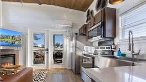 A modern kitchen with a stove, microwave, and sink, a dining area with a fire feature, and a large window. - Grace's Joy | 2 Bedrooms + Loft | Electric Fireplace (Fredericksburg)