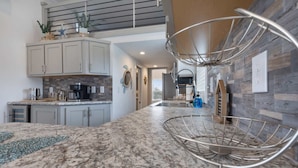 Una cucina moderna con piani in granito, forno integrato ed un originale scaffale in filo di metallo.