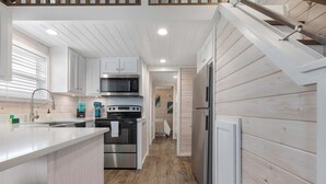 A modern kitchen with white cabinetry, a central island, stainless steel appliances, and wooden flooring. - The Geode (Fredericksburg)