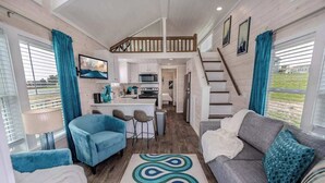 A spacious living area with a sofa, chairs, a kitchen, and a staircase leading to an upper level. - The Geode (Fredericksburg)