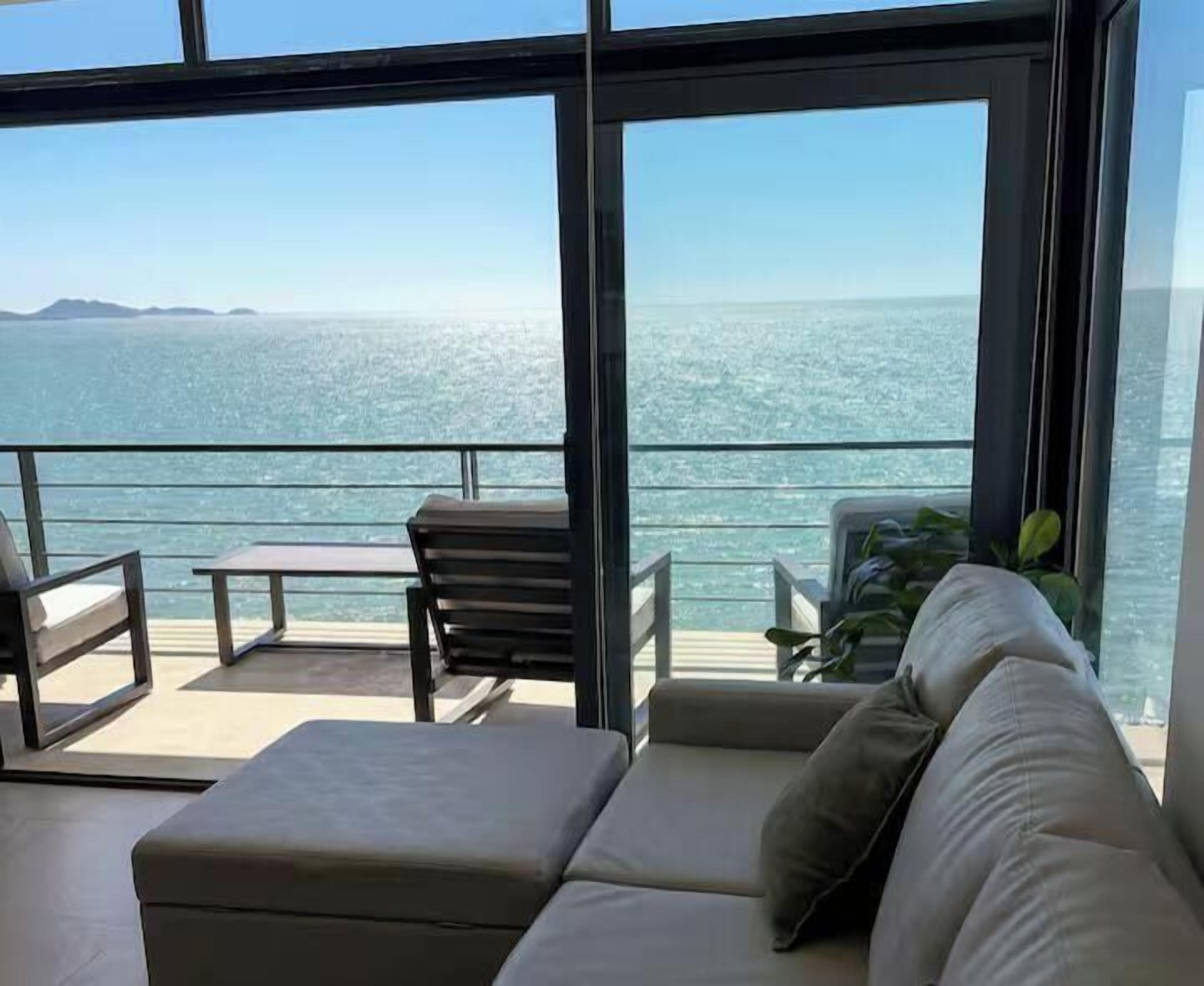 A modern room with a large glass window, a sofa, a small table, and a chair.