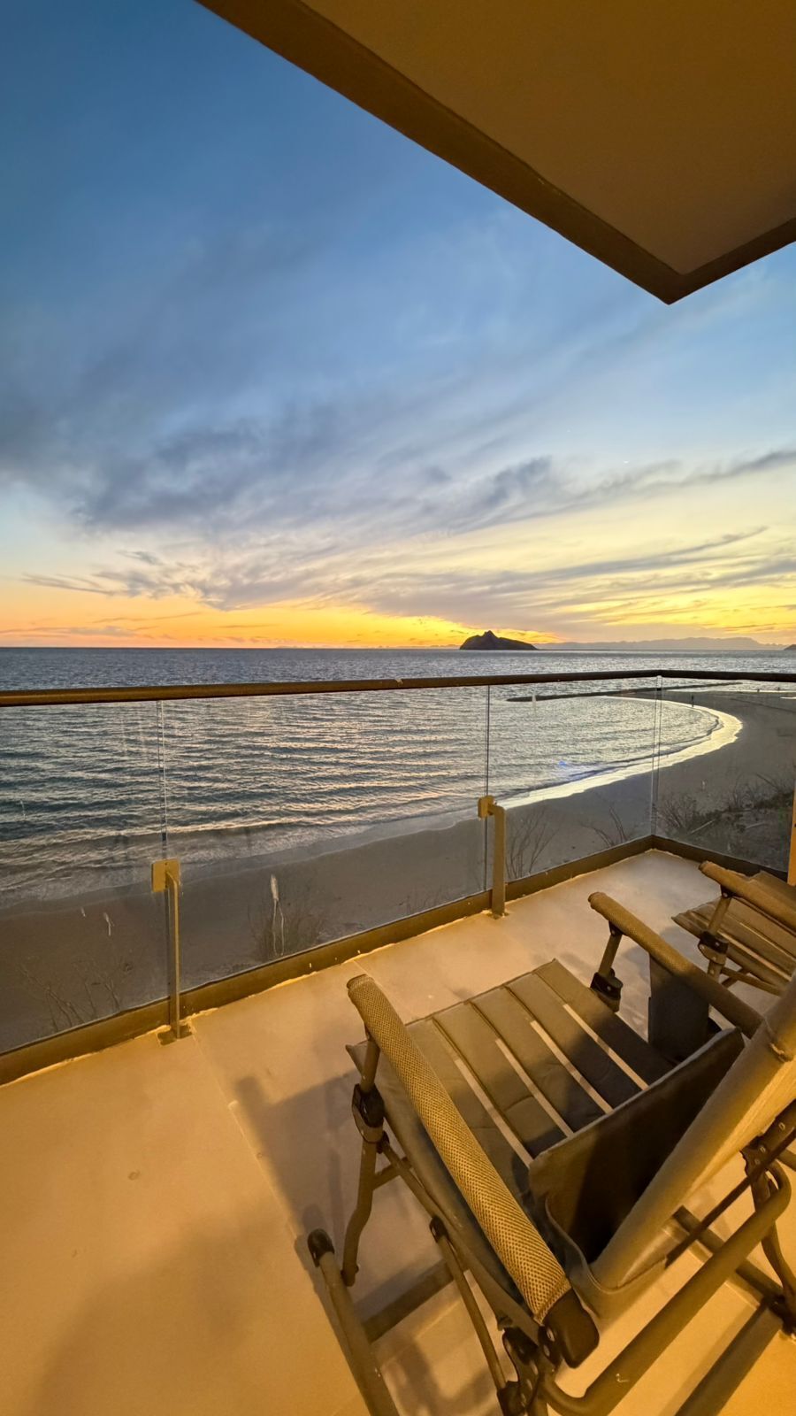 Un balcon avec vue sur la mer et sur le coucher de soleil. Il y a deux chaises et une table.