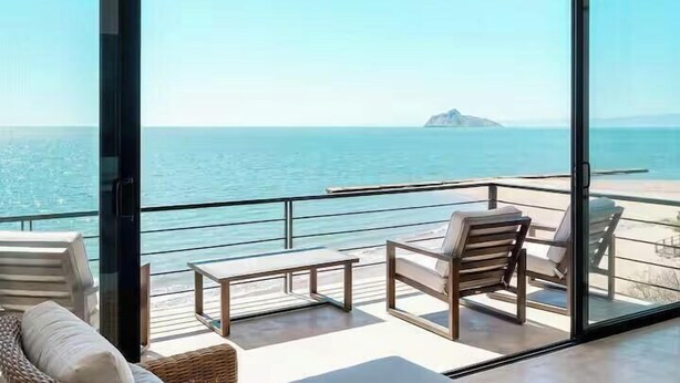 A balcony with a view of the sea, a small island, and a clear sky.