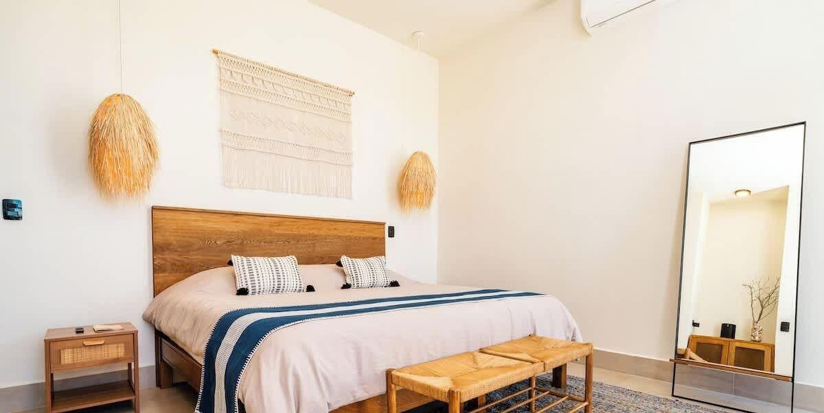 Une chambre à coucher avec un lit en bois, une table de chevet, un banc, un grand miroir et deux éléments de décoration murale.