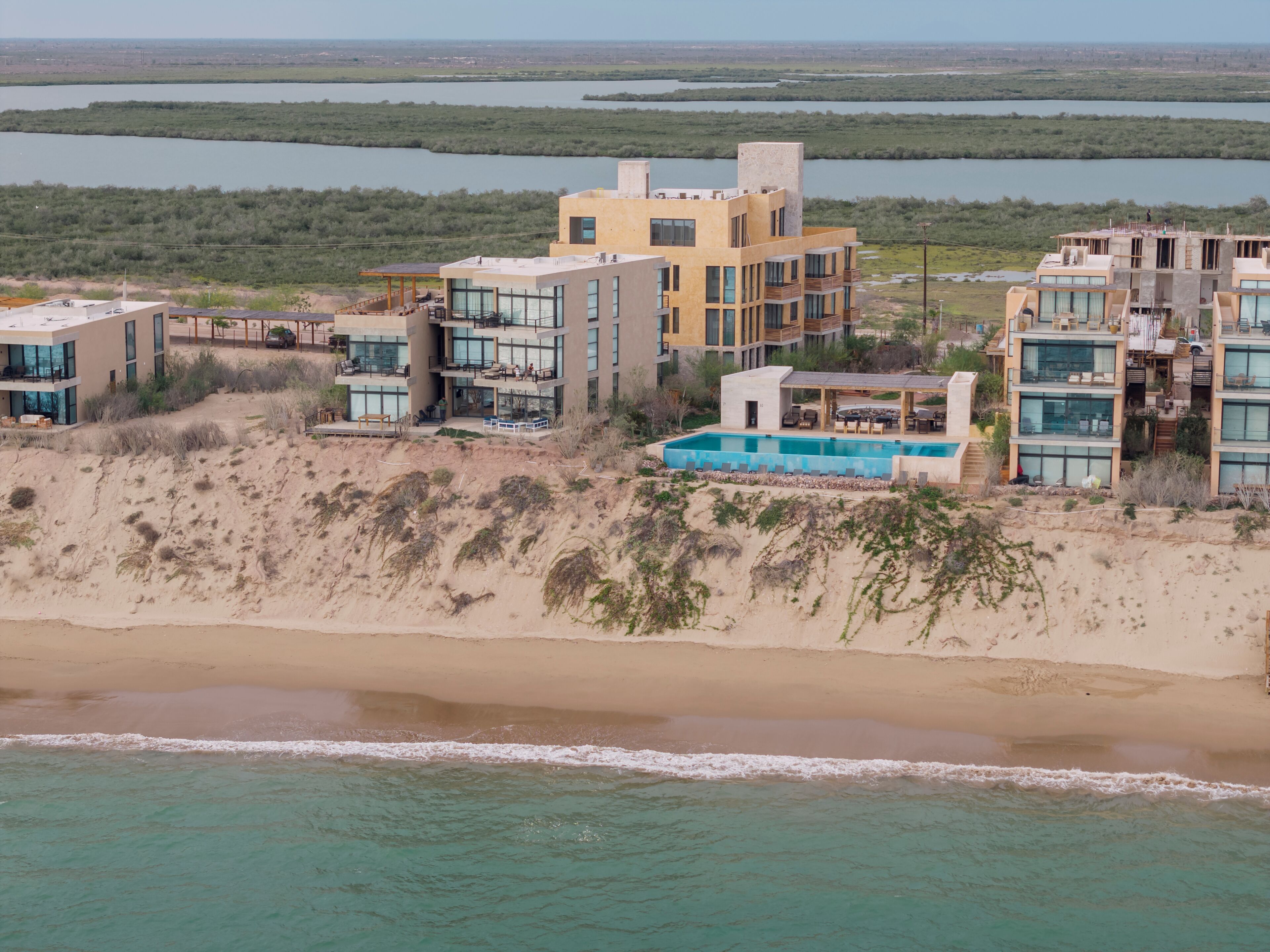 A coastal property with multiple buildings, a swimming pool, and a beach.