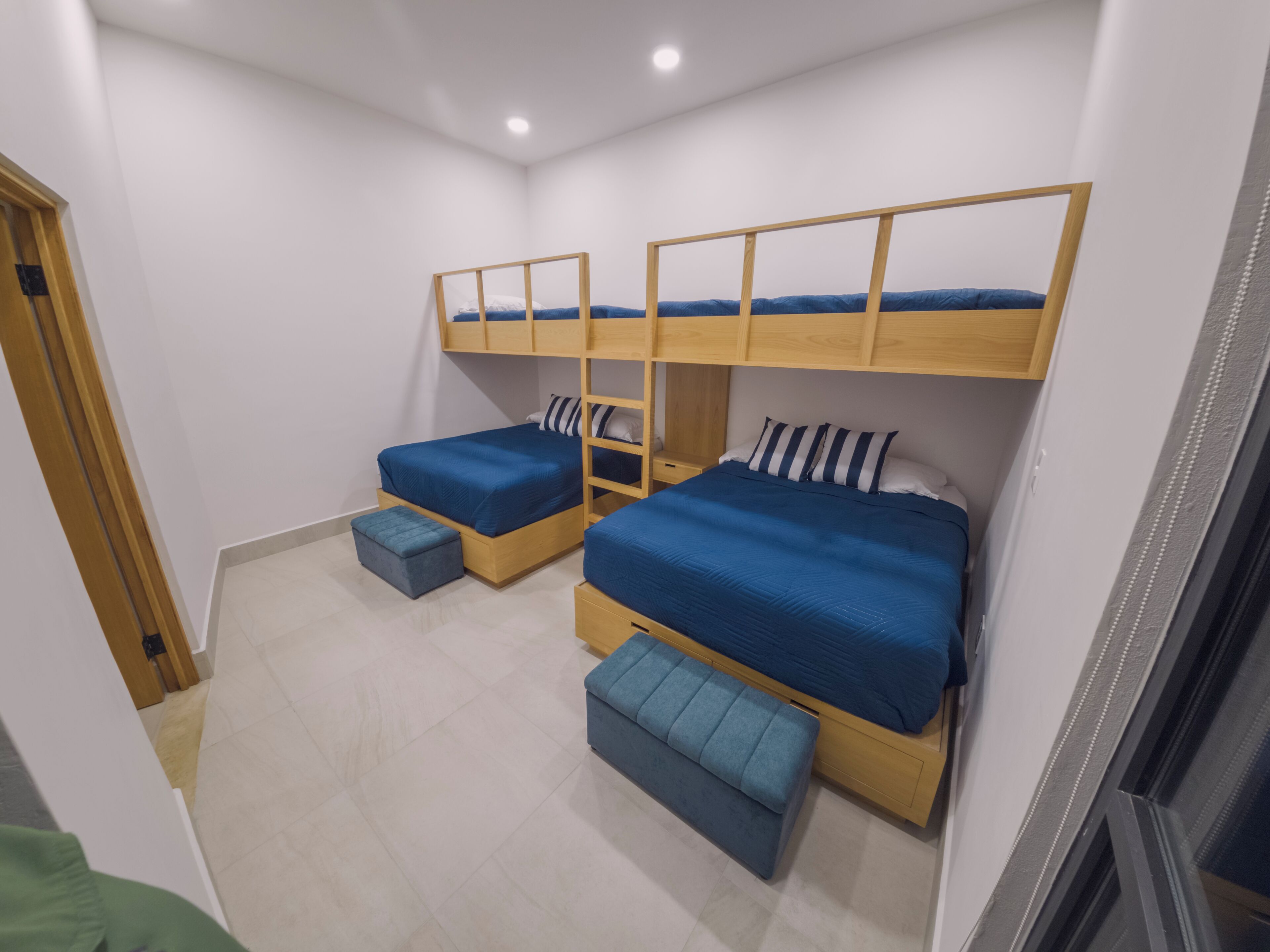 A room with bunk beds, a small bench, and a door.