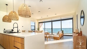A modern kitchen with a large island, wooden cabinets, and a view of the sea through large windows.