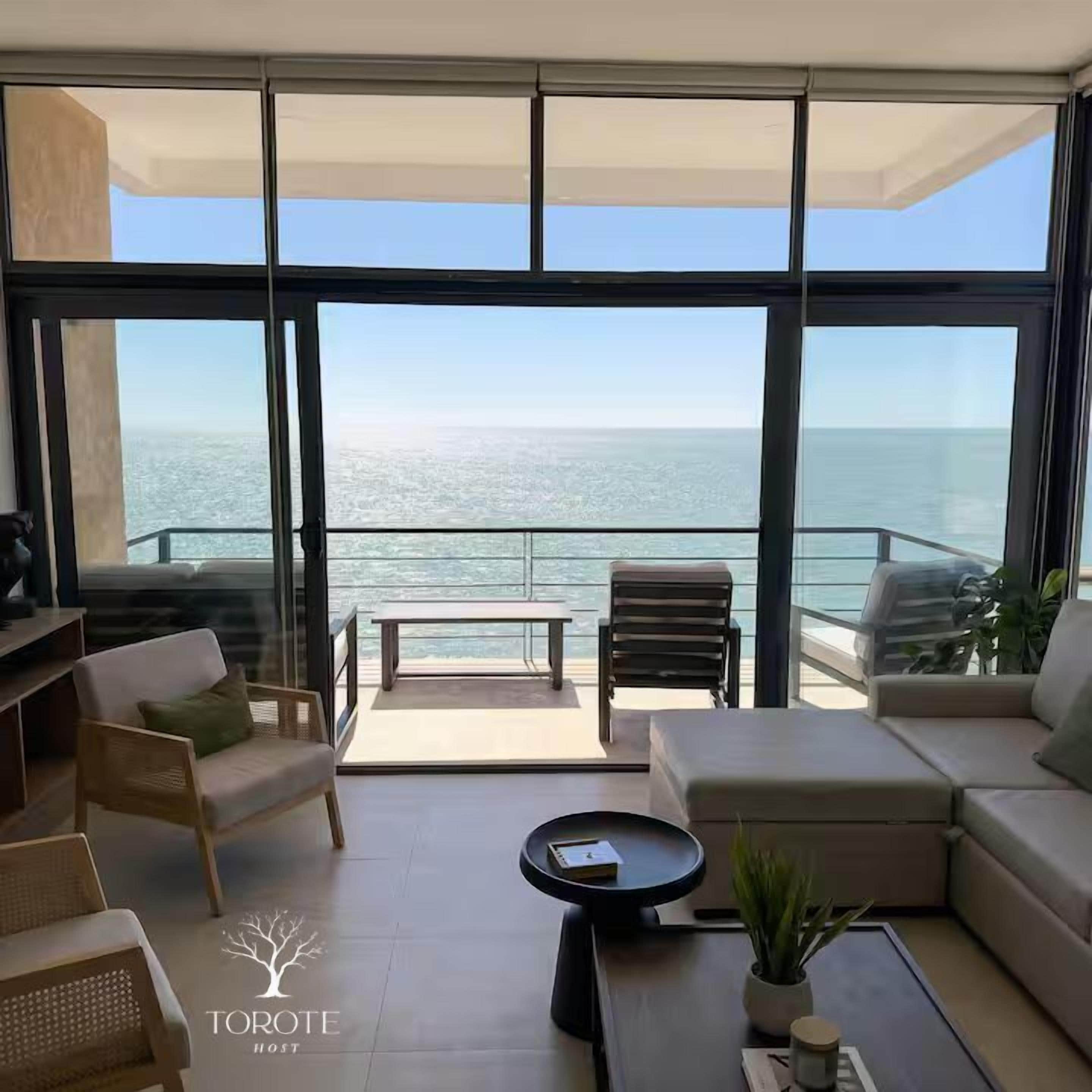 A modern living room with a view of the ocean, furnished with sofas, chairs, and a coffee table.