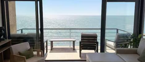 A modern living room with a view of the ocean, furnished with sofas, chairs, and a coffee table.