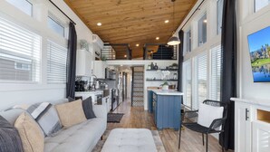 A spacious living area with a sofa, ottoman, and a dining area with a bar. There is a staircase leading to an upper level. - TXFirefly88 | Two Porches, Picnic Table (Fredericksburg)