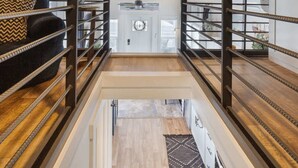 A modern interior with a wooden ceiling, a central light fixture, a black sofa with patterned cushions, and a view through a glass door. - TXFirefly88 | Two Porches, Picnic Table (Fredericksburg)