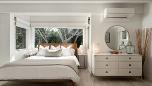 A bedroom with a bed, bedside tables, a dresser, a mirror, and an air conditioning unit.