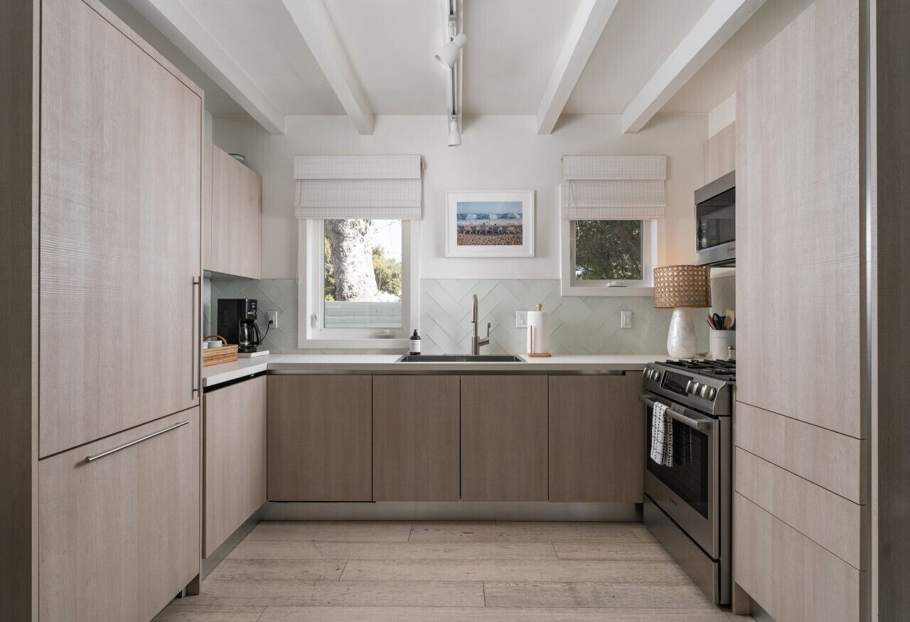 Een moderne keuken met lichte houten kastjes, een roestvrijstalen fornuis en een groot raam met uitzicht op de omgeving.