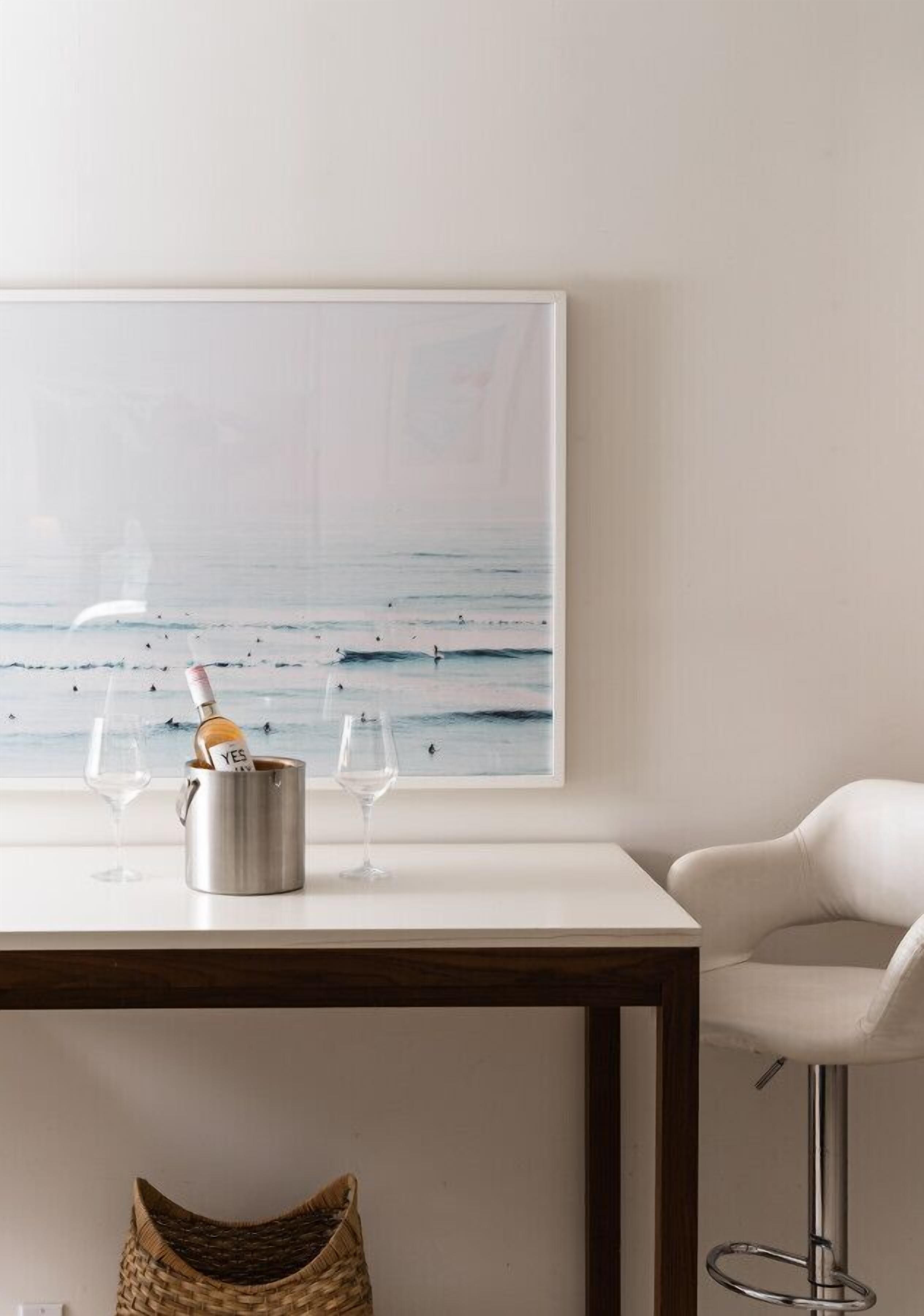 A modern interior with a white table, a framed seascape painting, a wine bottle, and two glasses.
