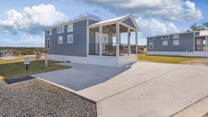 A modern single-story house with a covered porch and a small deck, surrounded by a well-maintained lawn and a clear sky. - Then Sings My Soul | Covered Porch & Fireplace! (Fredericksburg)