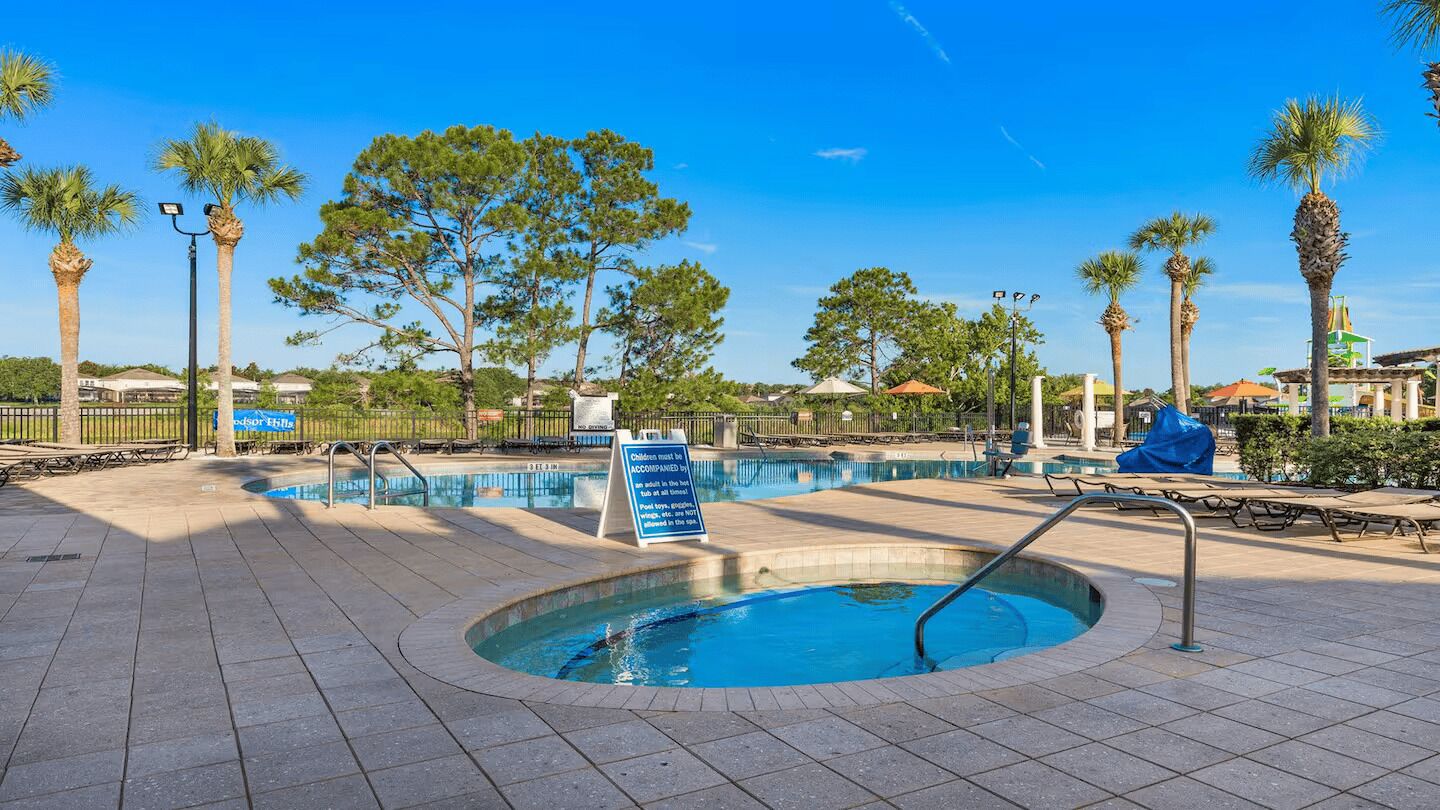 A swimming pool area with a hot tub, surrounded by palm trees and lounge chairs.