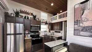 A modern kitchen with stainless steel appliances, wooden cabinets, and a cozy seating area with a cushioned bench and a pillow. - Comfortably Numb 223 (Fredericksburg)