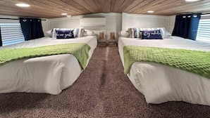 A room with two beds, each with a green blanket, white bedding, and matching pillows. There are ceiling lights and a window with curtains. - Comfortably Numb 223 (Fredericksburg)