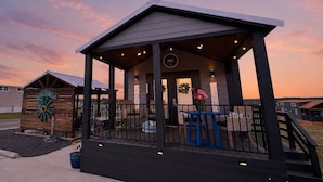 A wooden building with a covered porch, a sign reading 'WELCOME,' and a 'COZY' sign above the door. - Comfortably Numb 223 (Fredericksburg)