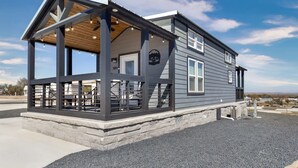 A two-story house with a covered porch, a wooden deck, and a stone foundation. - Tiny Treasure | 1.5 Baths | Sleeps 6 | Dual Porches (Fredericksburg)