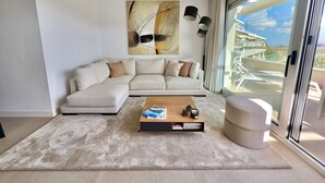 Een moderne woonkamer met een hoekbank, een salontafel en een groot raam met uitzicht op een brug en gebouwen.