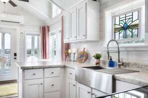 A kitchen with white cabinets, a stainless steel sink, a window with stained glass, and a ceiling fan. - Blue Skies | Tiny Home 41 at Firefly Resort (Fredericksburg)