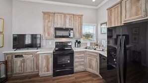 Una cucina con mobili in legno, un fornello nero, un forno a microonde e un frigorifero.