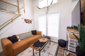 Ein moderner Wohnraum mit einem braunen Ledersofa, einem Couchtisch, einem Wandbild mit einer Landkarte, einem großen Fenster mit Jalousien und einer Treppe.