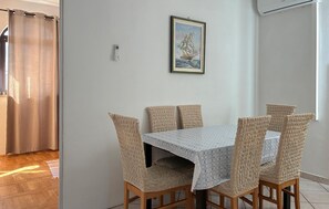 Ein Essbereich mit Tisch und Stühlen, einem gerahmten Bild an der Wand und einem Vorhang.