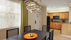 Une cuisine moderne avec des meubles en bois, un four à micro-ondes et un réfrigérateur. On y trouve une table à manger avec des chaises et une assiette de fruits.