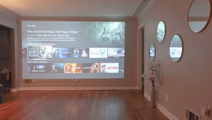 Un écran de projection diffusant une sélection de films dans une pièce dotée d’un plancher en bois et de miroirs décoratifs.