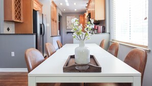 Un coin repas avec une longue table, des chaises en bois, un vase blanc orné de fleurs et des meubles de rangement en bois.