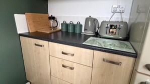 A kitchen with wooden cabinets, a black countertop, and various appliances including a coffee maker, kettles, and a toaster. - Meriden Apartment Retreat - Sleeps 7 - Near Nec (Solihull)
