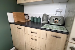 A kitchen with wooden cabinets, a black countertop, and various appliances including a coffee maker, kettles, and a toaster.