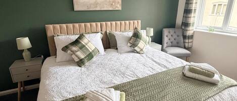 Un lit bien fait, recouvert d’une housse blanche matelassée, avec deux oreillers et un plaid vert.
