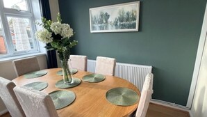 A dining area with a round wooden table, white chairs, and a vase with flowers. - Meriden Apartment Retreat - Sleeps 7 - Near Nec (Solihull)
