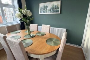 A dining area with a round wooden table, white chairs, and a vase with flowers.