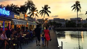 A waterfront restaurant with outdoor seating, palm trees, and a sunset sky. - Charming studio overlooking Saint-François marina, golf course, lagoon & beach on foot. (Saint-François)