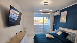 A modern bedroom with a bed, bedside table, and a TV mounted on the wall. - Charming studio overlooking Saint-François marina, golf course, lagoon & beach on foot. (Saint-François)